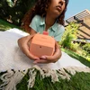 Bose SoundLink Micro (2nd Gen) portable Bluetooth speaker in Sunset Peach, held outdoors on a picnic blanket