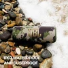 JBL Flip 6 portable Bluetooth speaker in Squad, on wet pebbles by the sea