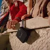 Marshall Willen portable Bluetooth speaker in Black and Brass, hanging from a hand by its strap