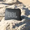 JBL Go Essential 2 portable Bluetooth speaker in Black, half buried in beach sand