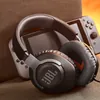 JBL Quantum 100 wired gaming headset in Black, resting on a sofa next to a handheld games console