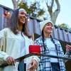 JBL Go 5 portable Bluetooth speaker in Red, on a railing with two friends outdoors