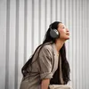 Sennheiser Momentum 4 Wireless noise cancelling headphones in Graphite, worn by a woman sitting against a wall
