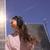 Sennheiser Momentum 4 Wireless noise cancelling headphones in Copper, worn outdoors by a woman in a striped shirt