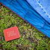 JBL Go Essential 2 portable Bluetooth speaker in Red, on the grass beside a tent